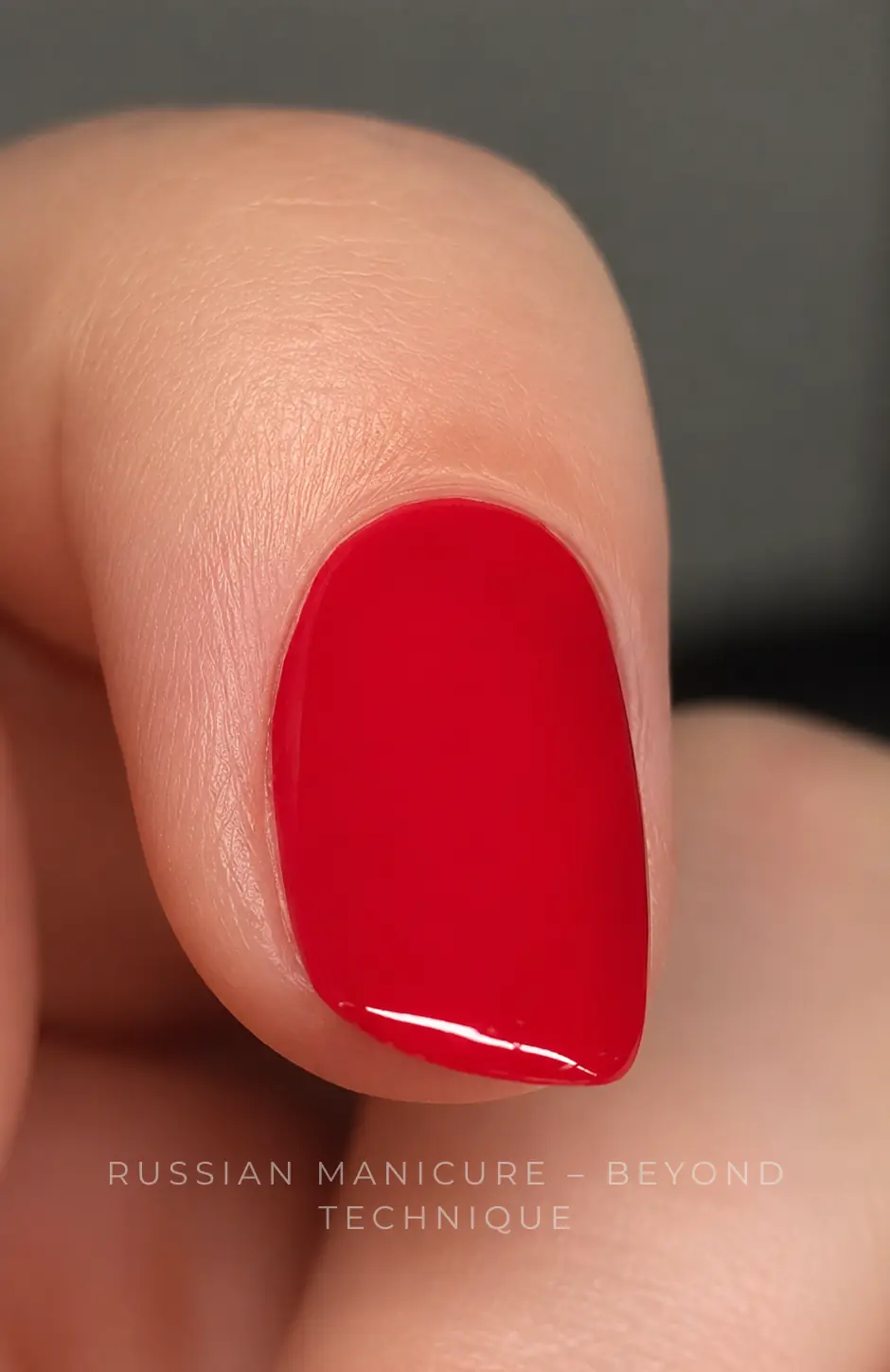 Macro photograph of a short red gel-polish nail on a finger, with smooth skin around the nail and the text Russian Manicure – Beyond Technique across the lower part of the image