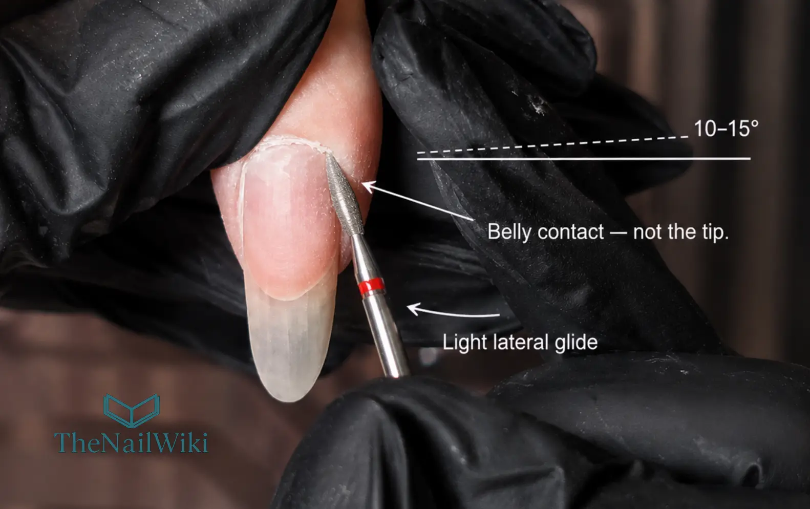 Diamond flame e-file bit held at the correct shallow angle working in the nail sinus — belly of the bit alongside the nail plate at approximately 10 to 15 degrees, tip pointing away