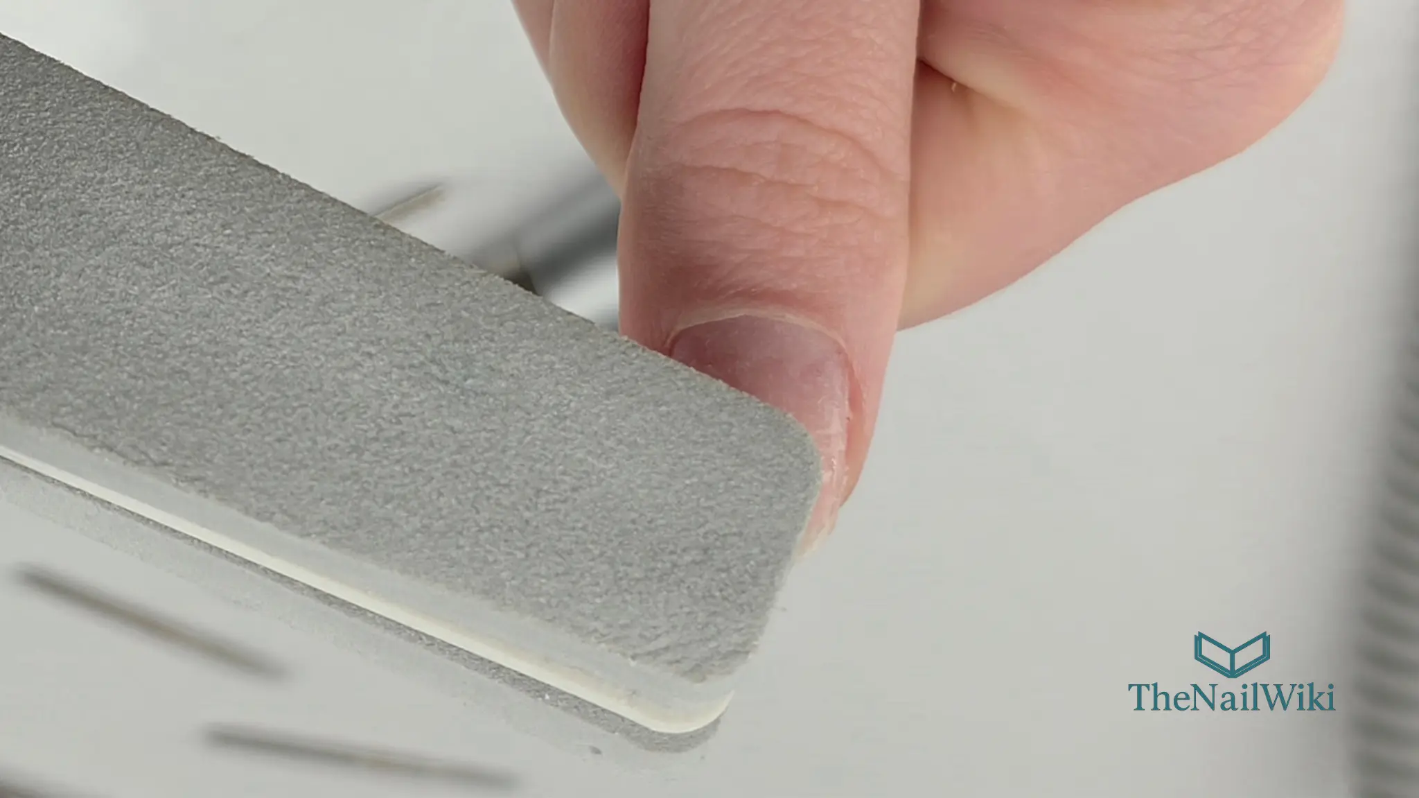 Close-up of a nail buffer being used on a natural nail in one direction only — a single controlled stroke across the nail plate