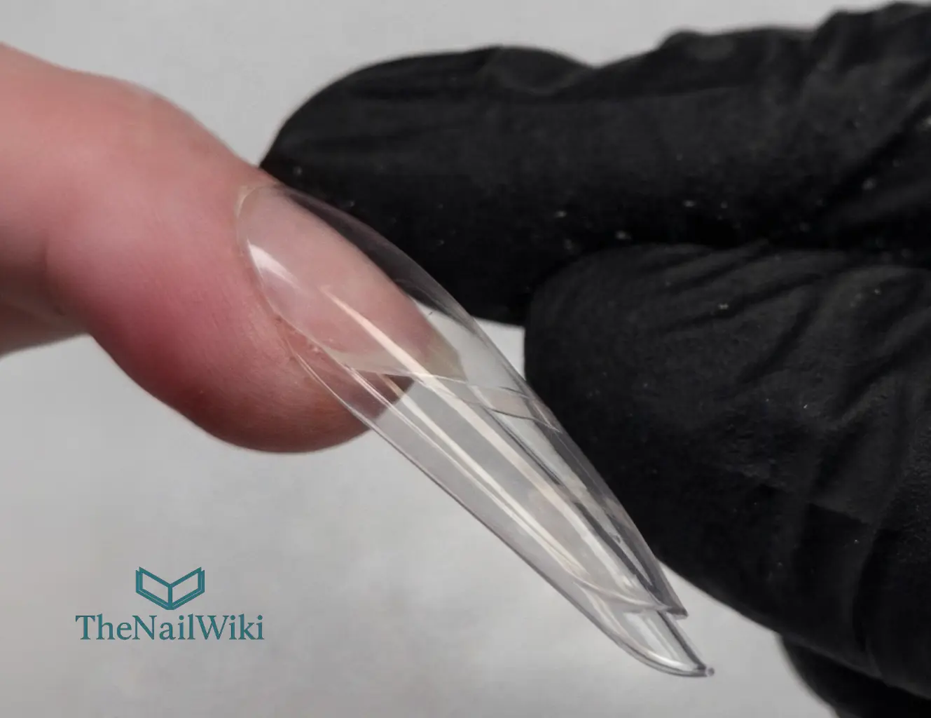 Sandwich dual form held against the nail from the side showing correct form fit — the two-part mould sitting against the natural nail before pressing