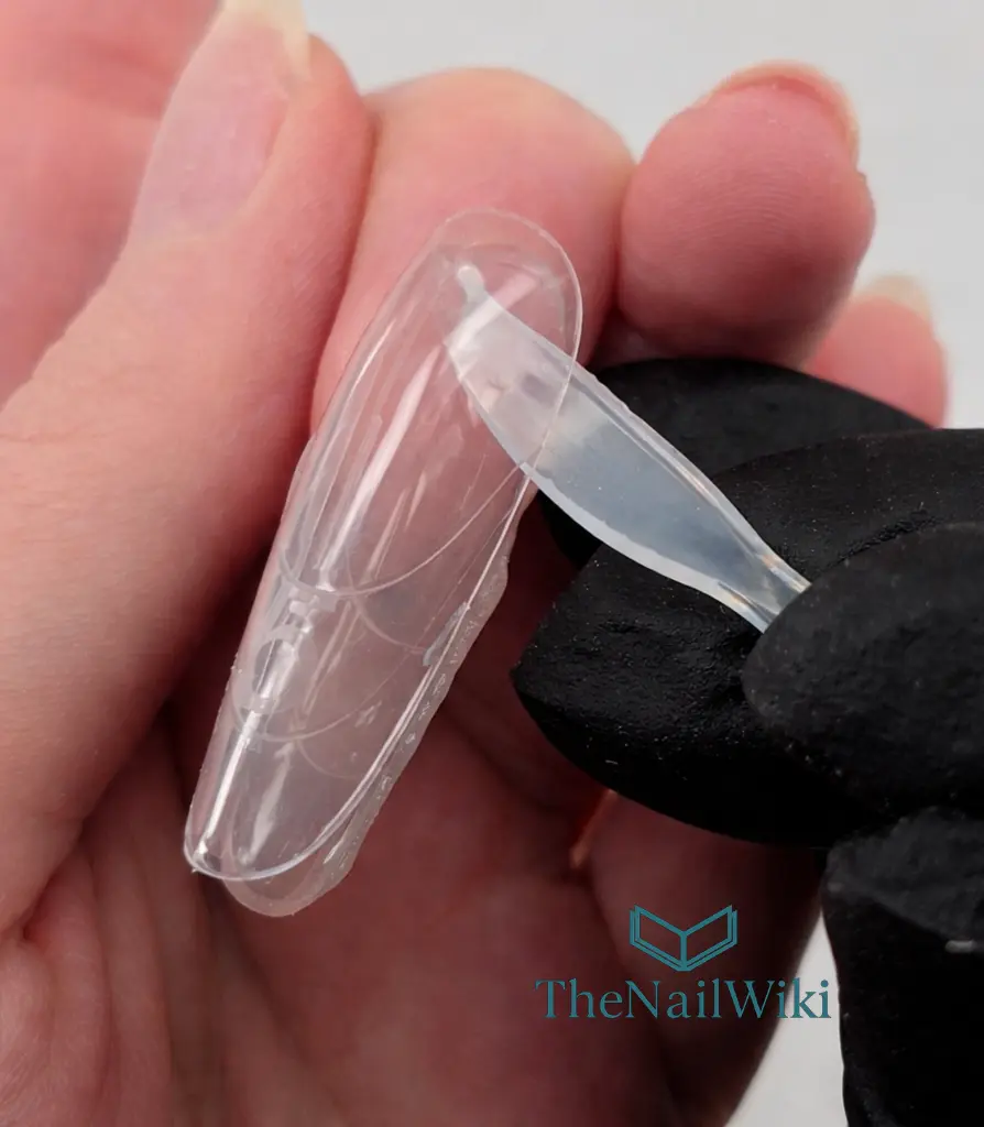 Sandwich dual form top mould being removed with a spatula after curing — revealing the finished nail enhancement underneath